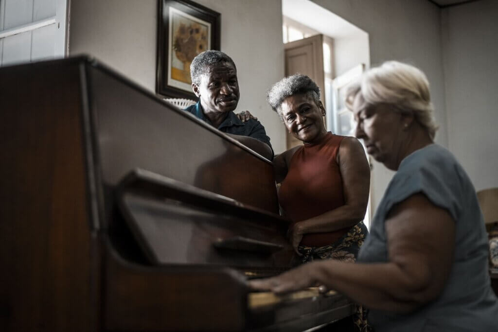 idosa tocando piano enquanto outros dois idosos estão ao seu lado